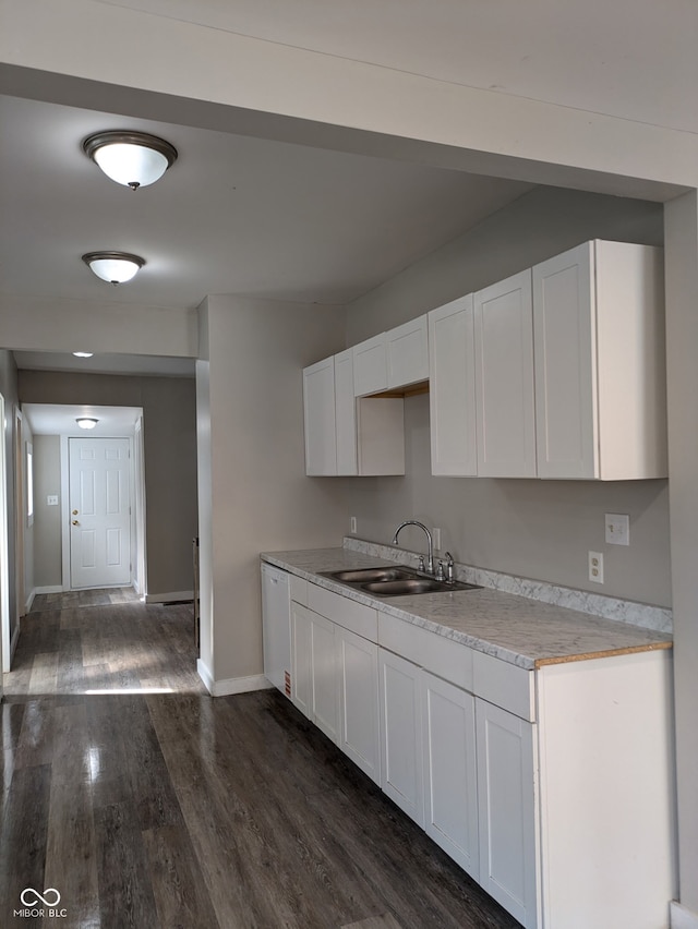 kitchen featuring white dishwasher, dark wood-style flooring, a sink, white cabinetry, and baseboards