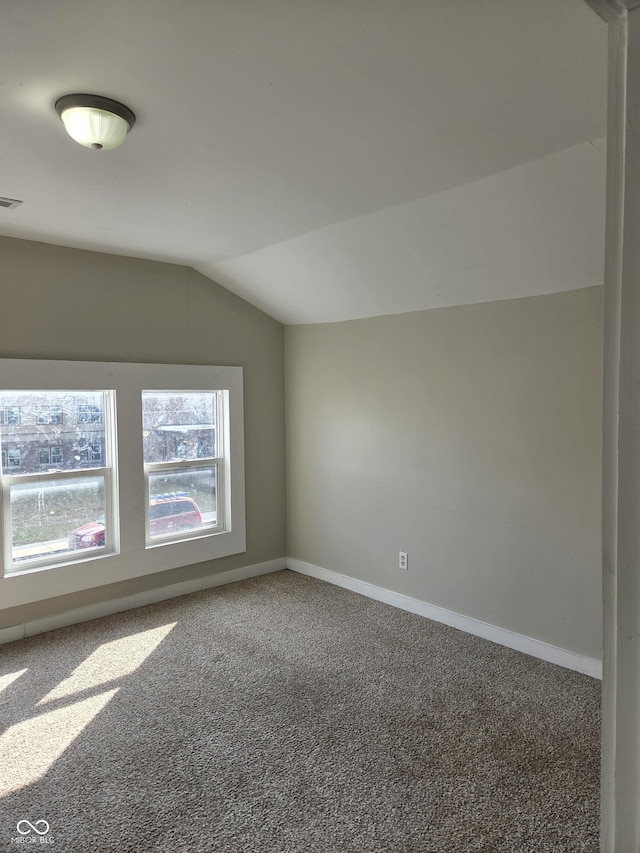 empty room with carpet floors, visible vents, vaulted ceiling, and baseboards