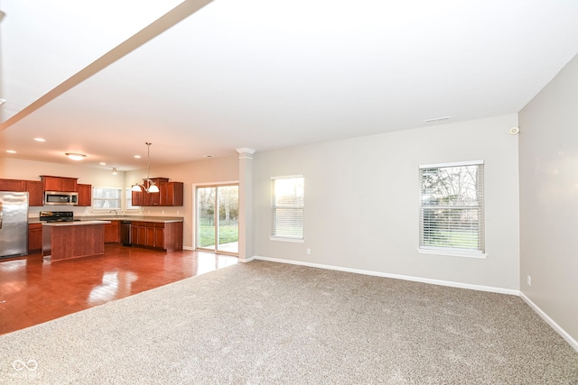 unfurnished living room featuring hardwood / wood-style floors, an inviting chandelier, a wealth of natural light, and ornate columns