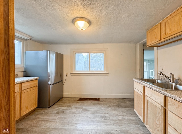 kitchen featuring stainless steel refrigerator, sink, light hardwood / wood-style flooring, a textured ceiling, and light brown cabinetry