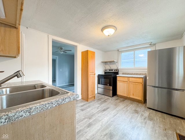 kitchen featuring appliances with stainless steel finishes, light brown cabinetry, a textured ceiling, sink, and light hardwood / wood-style floors