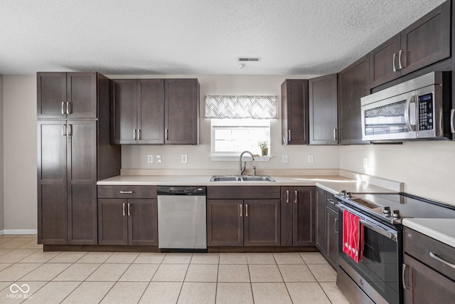 kitchen with appliances with stainless steel finishes, light tile patterned floors, dark brown cabinets, and sink