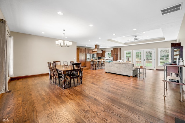 dining area featuring wood-type flooring, ceiling fan with notable chandelier, a tray ceiling, and french doors