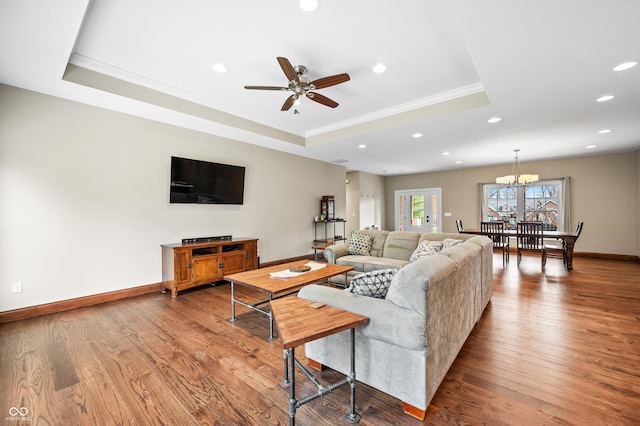 living room featuring a tray ceiling, ornamental molding, ceiling fan with notable chandelier, and hardwood / wood-style flooring