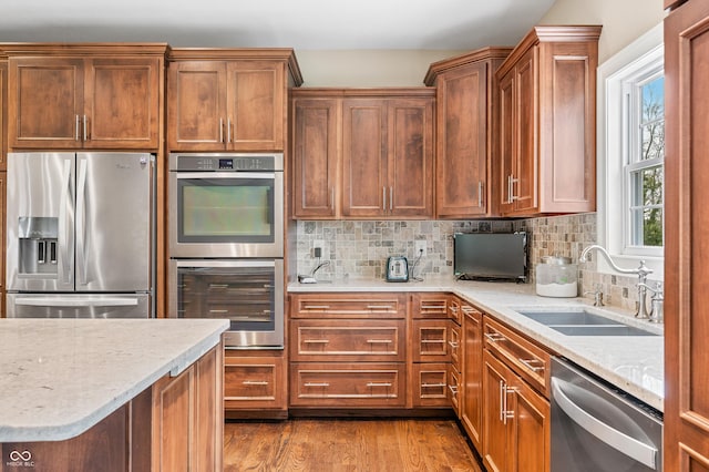 kitchen featuring sink, decorative backsplash, light stone countertops, appliances with stainless steel finishes, and light hardwood / wood-style floors