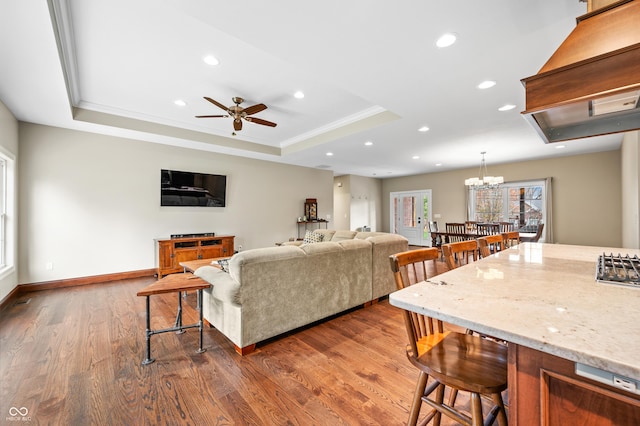 living room with ceiling fan with notable chandelier, dark hardwood / wood-style floors, a raised ceiling, and ornamental molding