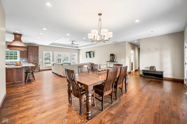 dining space featuring ceiling fan with notable chandelier, dark hardwood / wood-style floors, and a raised ceiling