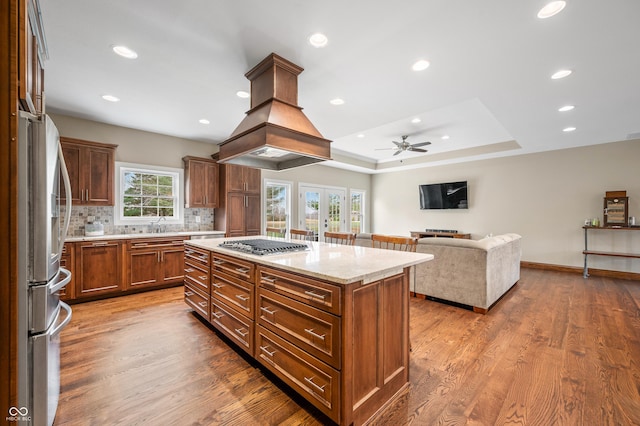 kitchen with hardwood / wood-style floors, a center island, light stone countertops, appliances with stainless steel finishes, and tasteful backsplash