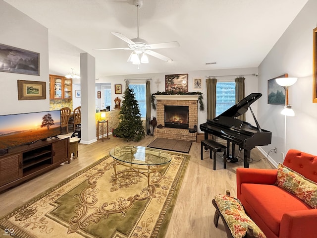 living room featuring a fireplace, light hardwood / wood-style flooring, ceiling fan with notable chandelier, and lofted ceiling