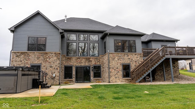 rear view of house with a hot tub, a wooden deck, a patio area, and a lawn