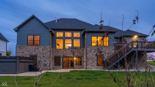 back house at dusk with a lawn, central AC unit, a hot tub, and a deck