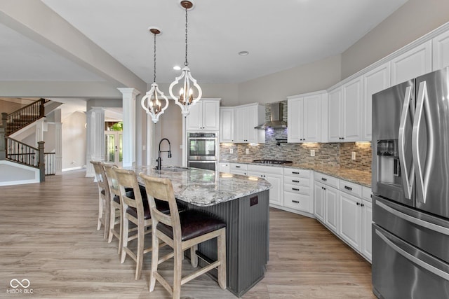 10346 Strongbow Rd, Fishers, IN 46040 - kitchen featuring appliances with stainless steel finishes, wall chimney exhaust hood, ornate columns, decorative backsplash, and light wood-style floors