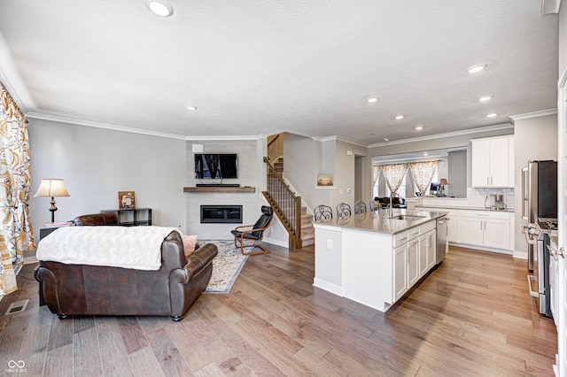 kitchen with light wood-type flooring, an island with sink, a large fireplace, white cabinetry, and stainless steel appliances