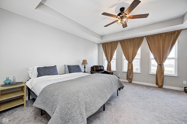 carpeted bedroom with ceiling fan, a tray ceiling, and multiple windows