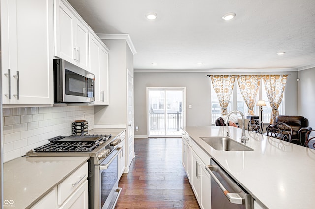 kitchen with appliances with stainless steel finishes, ornamental molding, dark wood-type flooring, sink, and white cabinetry