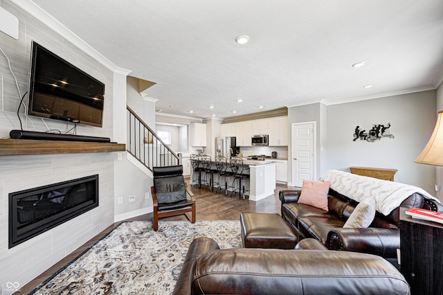 living room featuring a textured ceiling, ornamental molding, light hardwood / wood-style flooring, and a tiled fireplace