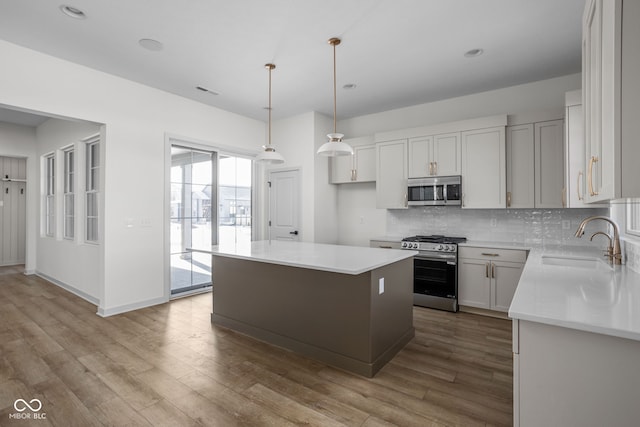 kitchen with appliances with stainless steel finishes, decorative light fixtures, white cabinetry, sink, and a center island