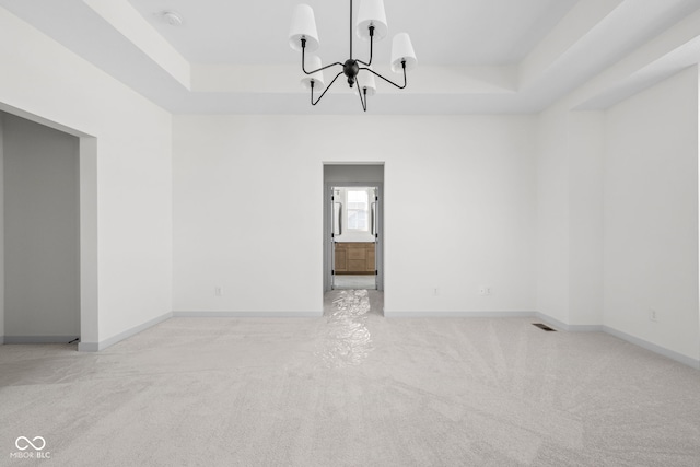 empty room featuring light carpet, a notable chandelier, and a raised ceiling