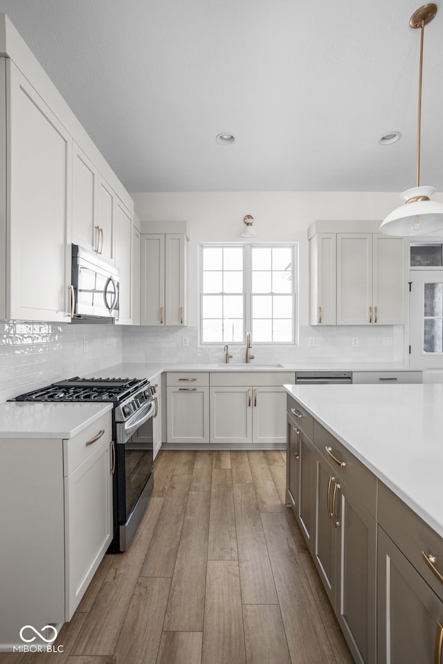 kitchen with appliances with stainless steel finishes, sink, backsplash, hanging light fixtures, and light wood-type flooring