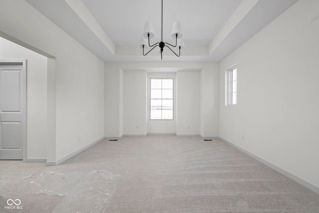 empty room featuring an inviting chandelier, light colored carpet, and a tray ceiling