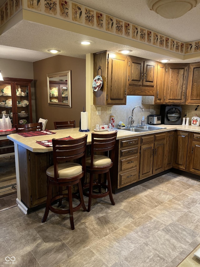 kitchen with sink, a kitchen breakfast bar, backsplash, kitchen peninsula, and a textured ceiling