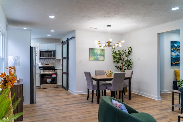 dining area featuring a textured ceiling, a barn door, an inviting chandelier, and light hardwood / wood-style flooring