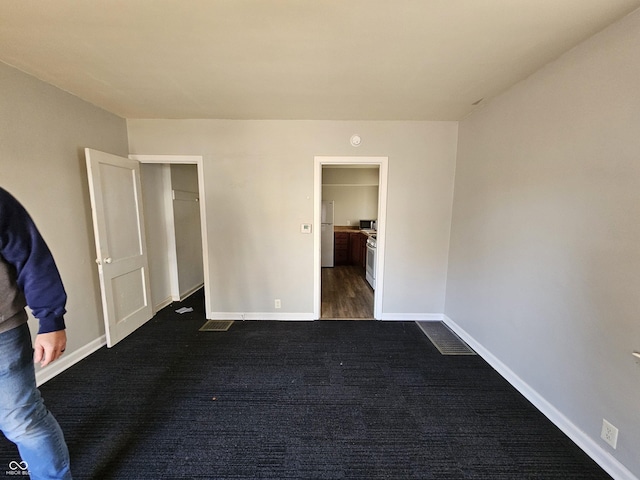 unfurnished bedroom with dark colored carpet and stainless steel fridge