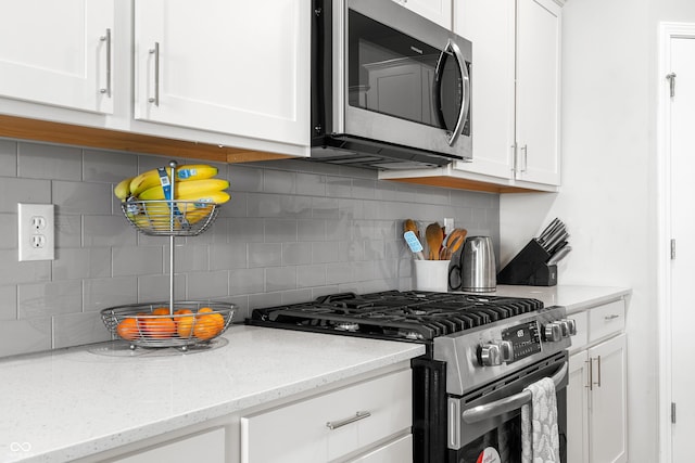 kitchen with white cabinets, appliances with stainless steel finishes, backsplash, and light stone countertops