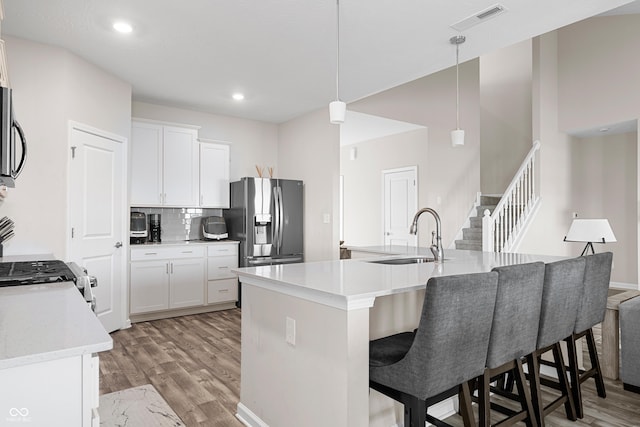 kitchen with a center island with sink, sink, decorative light fixtures, white cabinetry, and stainless steel appliances