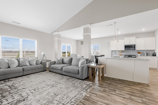 living room featuring vaulted ceiling, decorative columns, sink, and light hardwood / wood-style flooring