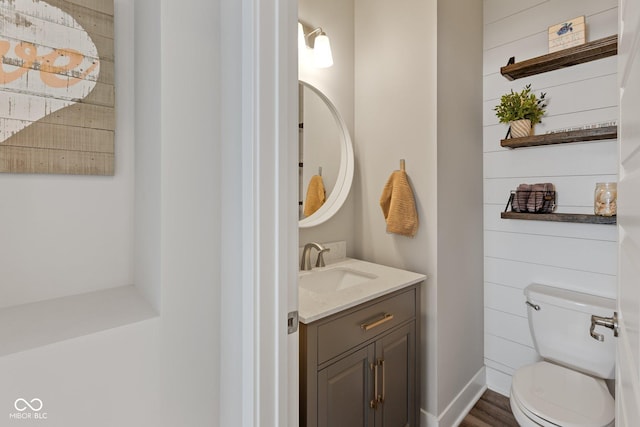 bathroom with toilet, vanity, wood walls, and hardwood / wood-style floors