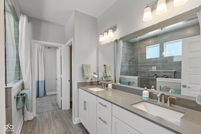 bathroom with a textured ceiling, tiled shower, and vanity