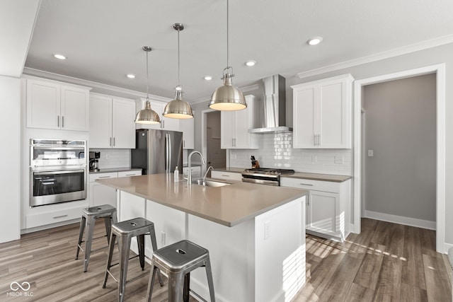 kitchen featuring pendant lighting, wall chimney range hood, white cabinetry, appliances with stainless steel finishes, and sink