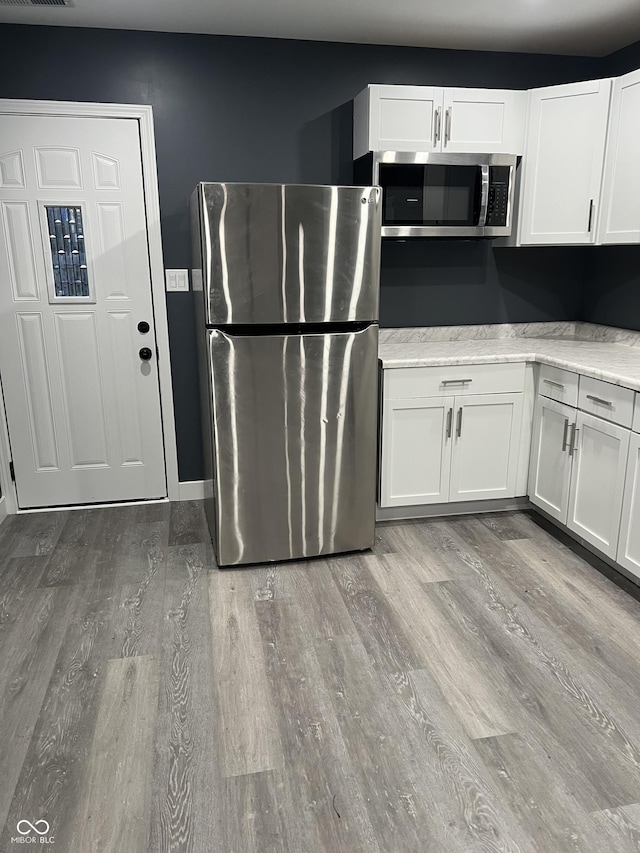 kitchen with white cabinets, appliances with stainless steel finishes, and light hardwood / wood-style flooring