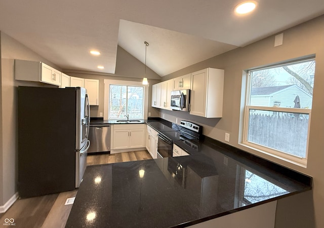 kitchen with stainless steel appliances, decorative light fixtures, white cabinetry, lofted ceiling, and dark stone countertops