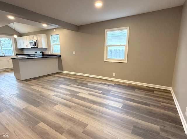 kitchen featuring hardwood / wood-style floors, appliances with stainless steel finishes, kitchen peninsula, white cabinets, and decorative light fixtures