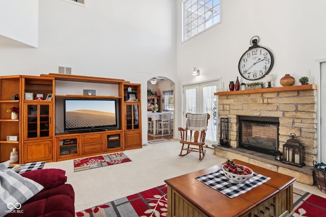 carpeted living room with ceiling fan, a fireplace, a towering ceiling, and french doors