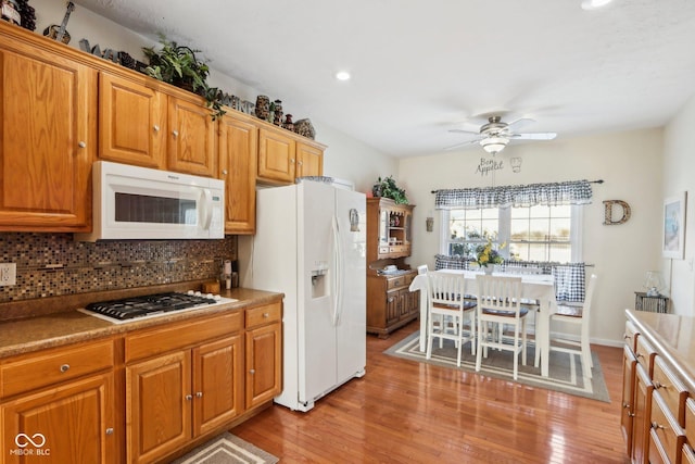 kitchen featuring decorative backsplash, ceiling fan, white appliances, and light hardwood / wood-style flooring