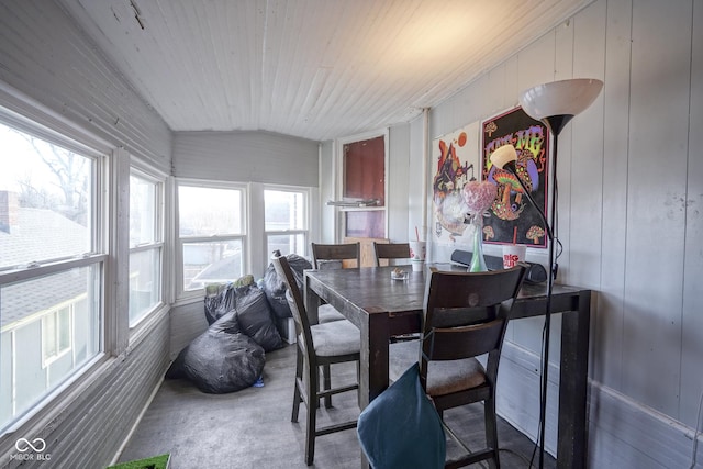 dining space with a healthy amount of sunlight, lofted ceiling, wooden walls, and concrete flooring