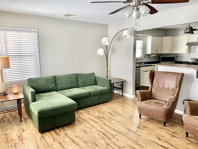 living area featuring light wood finished floors, baseboards, visible vents, and a ceiling fan