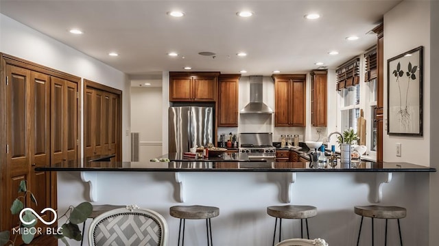 kitchen with wall chimney exhaust hood, kitchen peninsula, a breakfast bar area, and appliances with stainless steel finishes