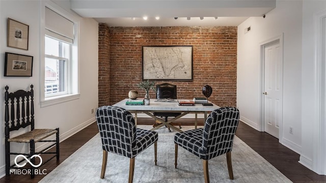 home office with dark wood-type flooring and brick wall