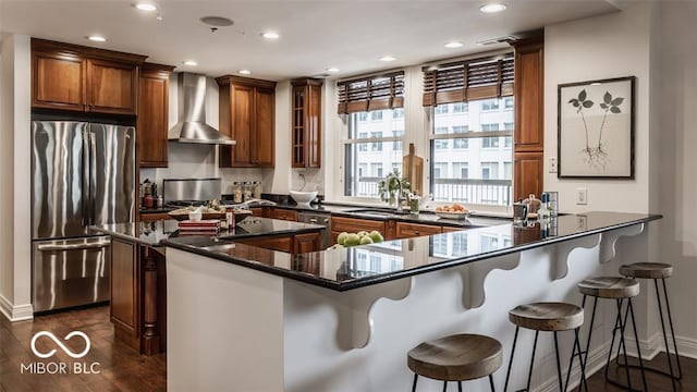 kitchen with appliances with stainless steel finishes, wall chimney exhaust hood, sink, dark hardwood / wood-style floors, and a breakfast bar area