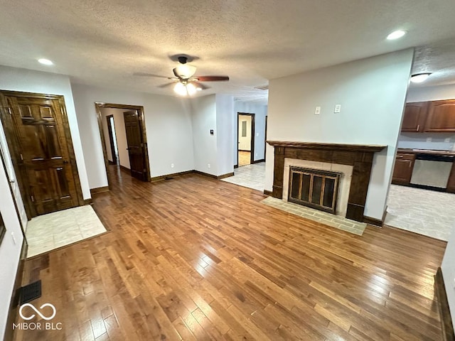 unfurnished living room featuring a tile fireplace, a textured ceiling, light wood-type flooring, and ceiling fan