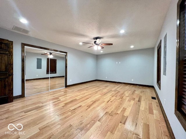 unfurnished room featuring electric panel, light hardwood / wood-style floors, and a textured ceiling