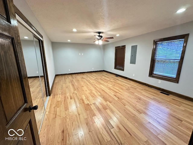 unfurnished bedroom featuring electric panel, ceiling fan, light hardwood / wood-style flooring, and a textured ceiling