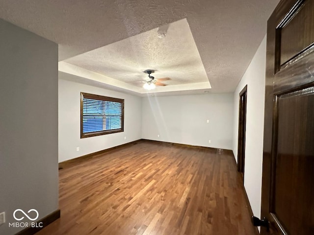 empty room with hardwood / wood-style floors, ceiling fan, a raised ceiling, and a textured ceiling