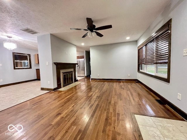 unfurnished living room featuring wood-type flooring, ceiling fan with notable chandelier, and a textured ceiling