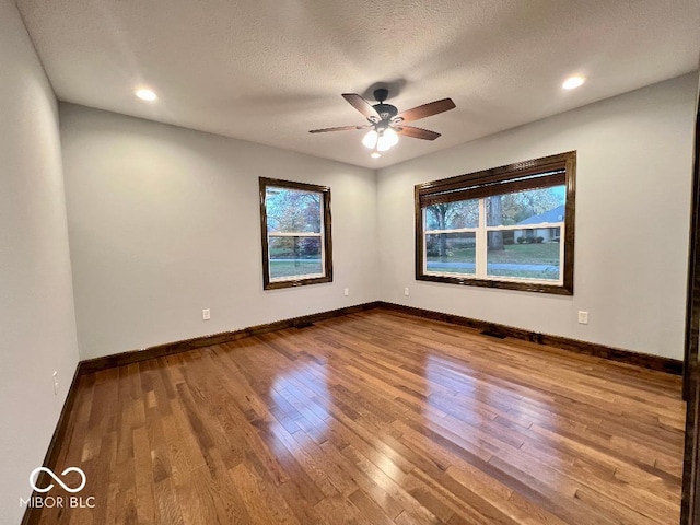 empty room with ceiling fan, wood-type flooring, a textured ceiling, and a wealth of natural light