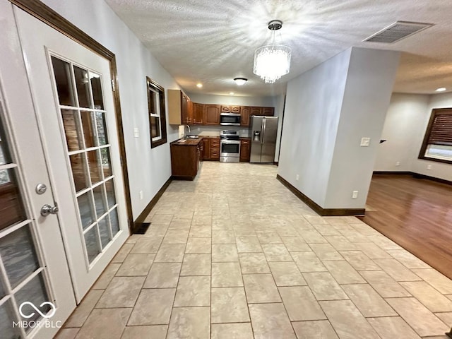 kitchen with a chandelier, decorative light fixtures, light hardwood / wood-style floors, a textured ceiling, and appliances with stainless steel finishes